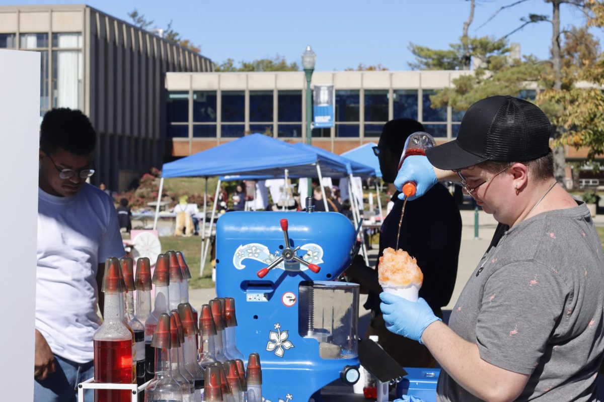 Alex Sausman, a senior in marketing, and the owner of Artic Ice making a snow cone for Elian Encarnacion, a junior in business analytics, at the Small Business Fair in the Library Quad Saturday.