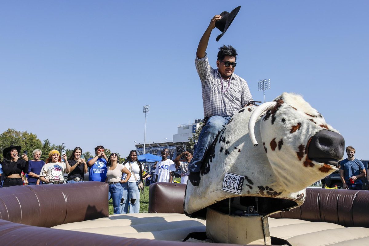 Hunter Mendoza, a junior accounting major, holds on to the mechanical bull as friends and fellow students cheer him on at the EIU tailgate outside the O'Brien Field Saturday afternoon. He said back home, he went to several rodeos so he had all the necessary apparel items for the western homecoming theme. Mendoza said he is very excited for his second homecoming.